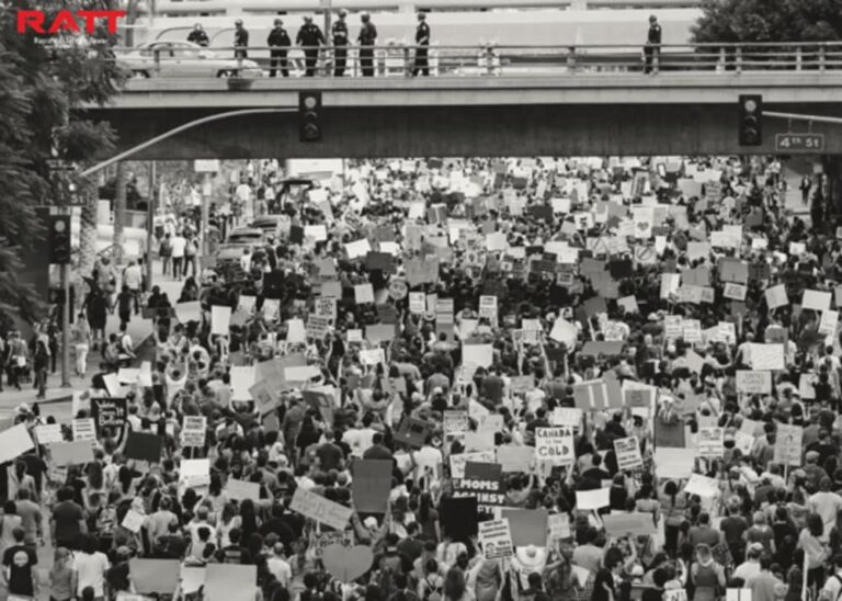 Law enforcement monitors large crowd from bridge during daytime protest.
