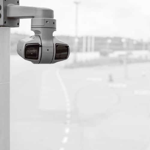 Grey Axis Q6225-LE ptz surveillance camera with wiper hanging upside down on concrete pole monitoring parking lot with blurry background