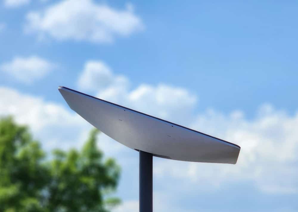 Starlink satellite dish against a blue sky with trees in the background